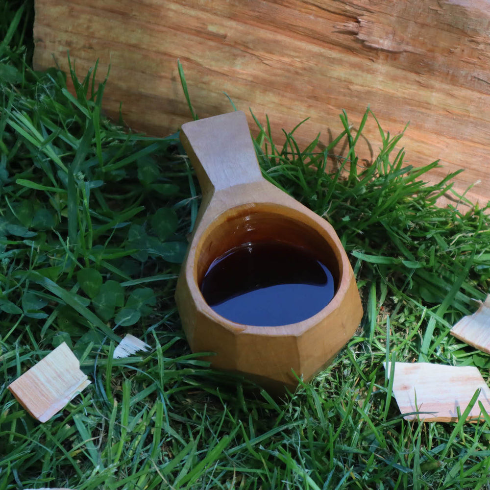 Wooden cup with dark liquid on grass