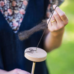 Person holding a drop spindle and yarn with a blurred green background