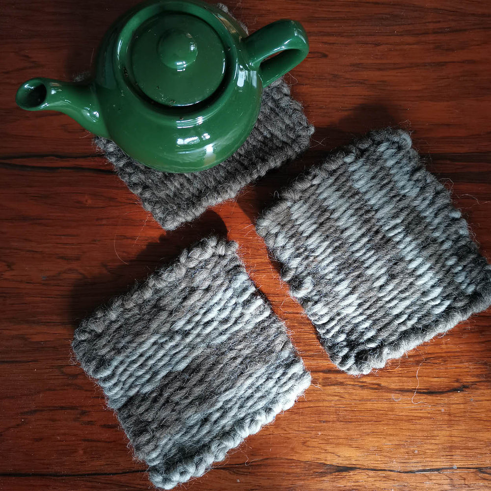 Green teapot on frame loom weave knitted coasters on a wooden surface