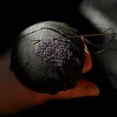 Close-up of a darning mushroom with black material and hand darned stitches with a needle piercing it, held by a hand.