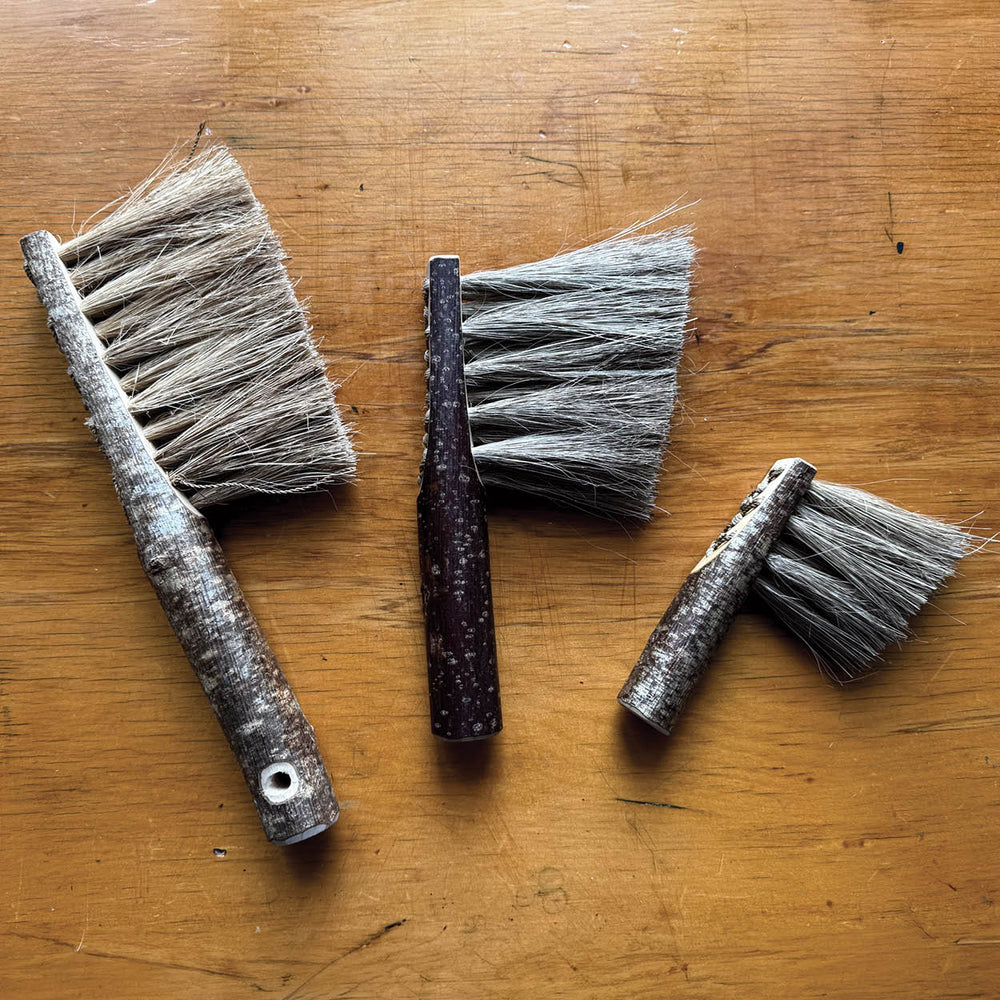Set of three brushes with bristle heads on a wooden surface.