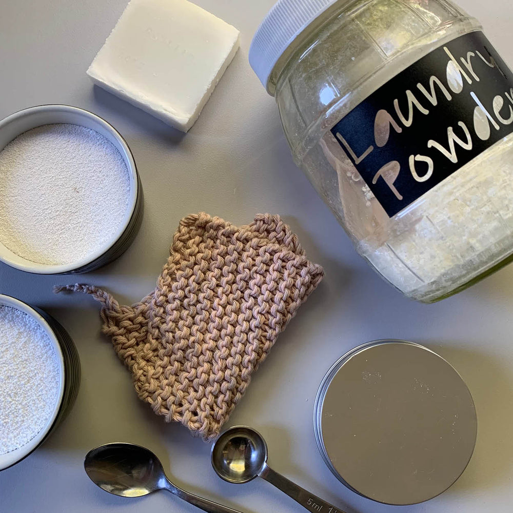 Jars of laundry powder and baking soda, a scrubber, and measuring spoons on a light surface.