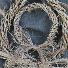 Woven ti kouka wreath with bow on a textured surface