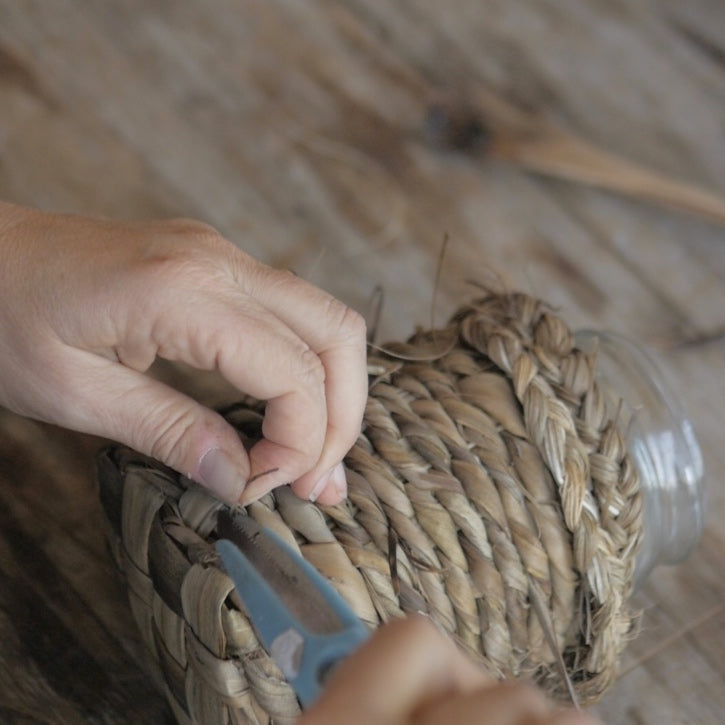 Hands holding scissors cutting the ends of tī kōuka from a wooven basket, working on a brown wooden table.