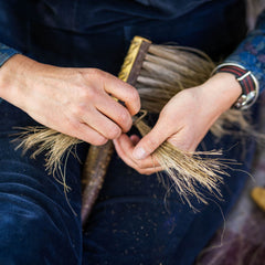Person holding a brush with straw bristles, wearing blue clothes.