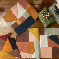 Patchwork fabric with geometric patterns on a wooden surface, surrounded by sewing materials.