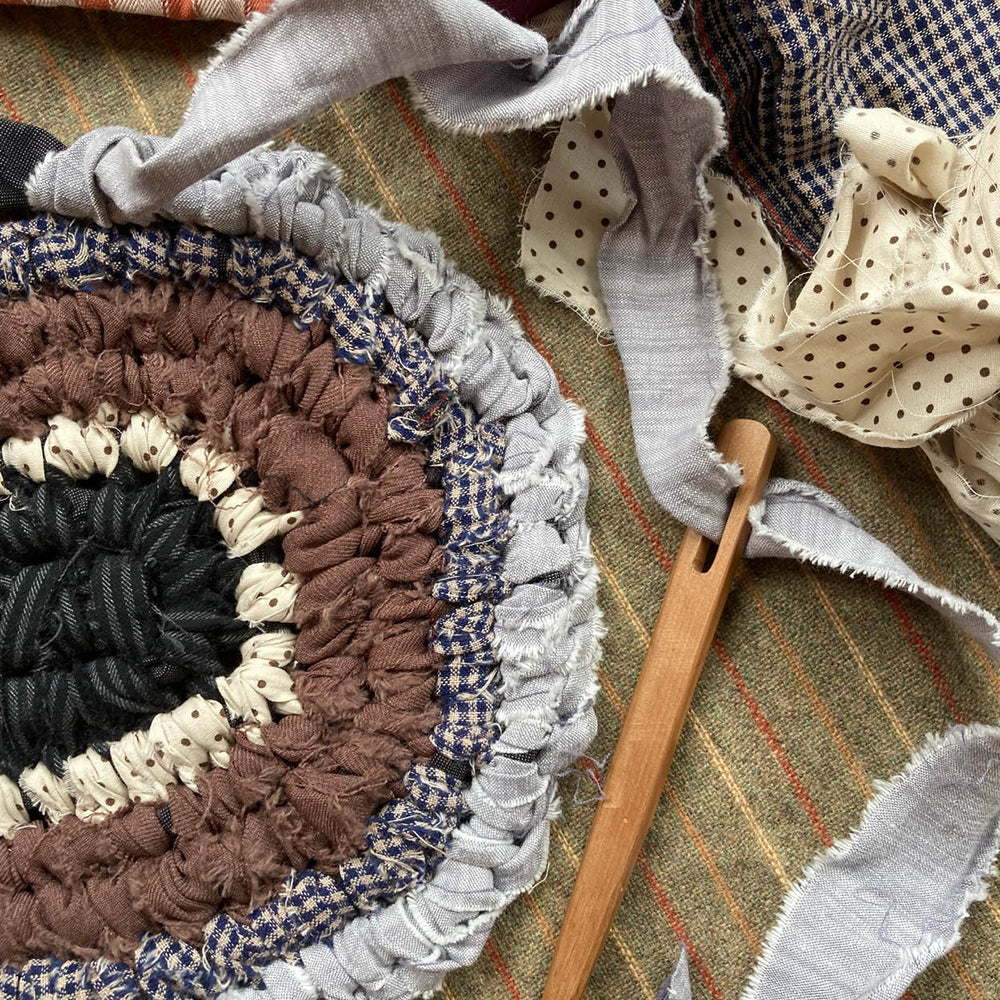 Handmade fabric rug with wooden tool on a plaid fabric background