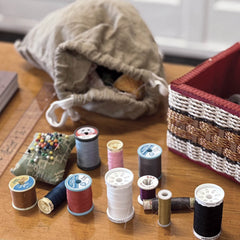 Spools of thread and sewing tools on a wooden surface with a fabric bag in the background.