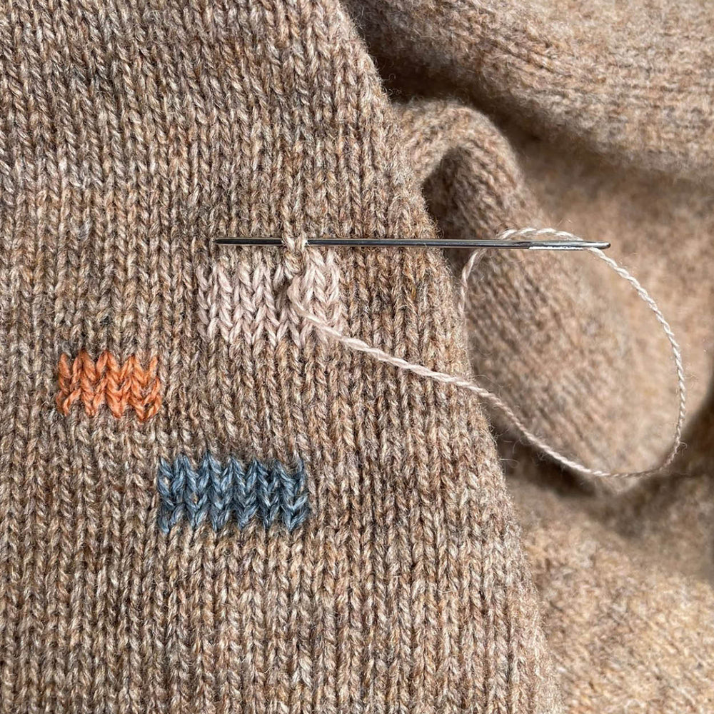 Close-up of a knitted fabric with a needle and thread, featuring small embroidered designs.